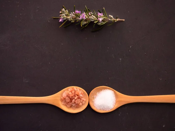 Cucharas de madera con sal marina común y sal rosada del Himalaya y una ramita de romero en un plato de pizarra — Foto de Stock