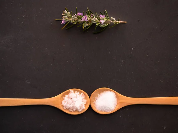 Cucharas de madera con sal marina común y copos de flores de sal en un plato de pizarra — Foto de Stock