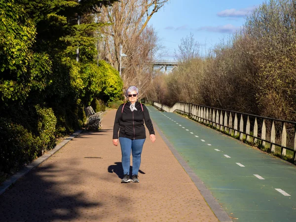 A magas rangú nő, fehér hajú hallgató séta egy városi parkban — Stock Fotó