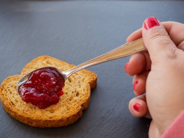 Bir dilim tost üzerinde bir kaşık ile kırmızı ahududu reçel bulaşmış boyalı çivi ile bir kadın