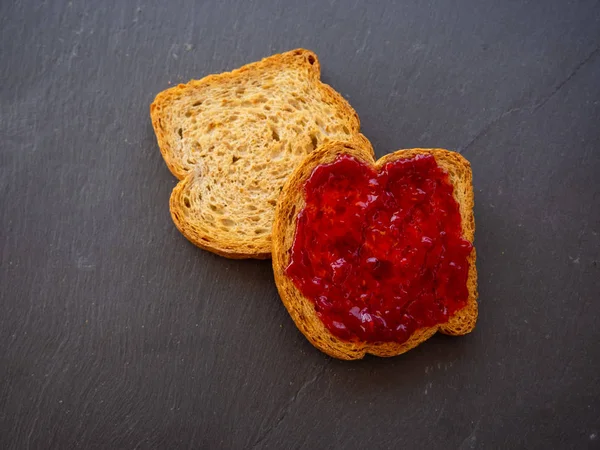 Dos rebanadas de tostadas con mermelada de frambuesa en un plato de pizarra —  Fotos de Stock