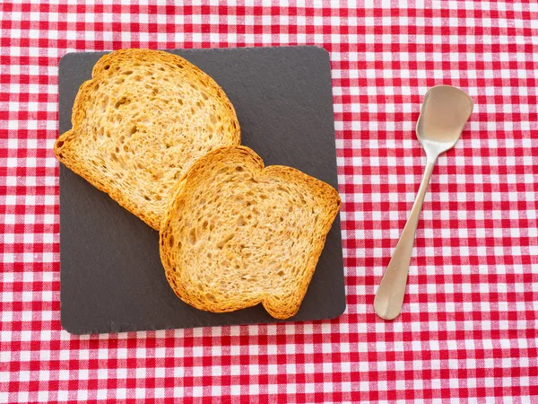 Two slices of toast on a slate plate, one old spoon and tablecloth vintage style — Stock Photo, Image