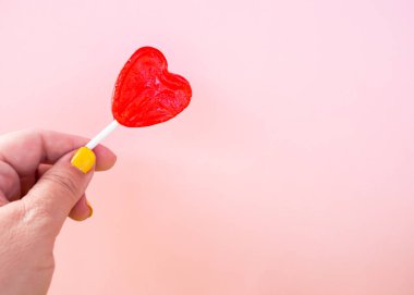 Elinde kırmızı lolipop ve pastel pembe arka plan ile sarı boyalı çivi ile bir kadın