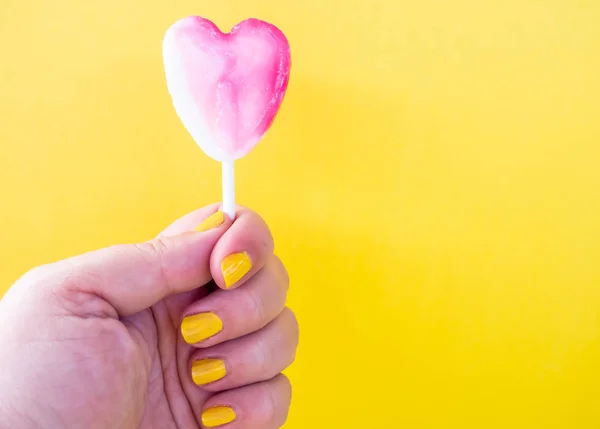 Een vrouw met geel geschilderde nagels met een lolly in haar hand en gele achtergrond — Stockfoto