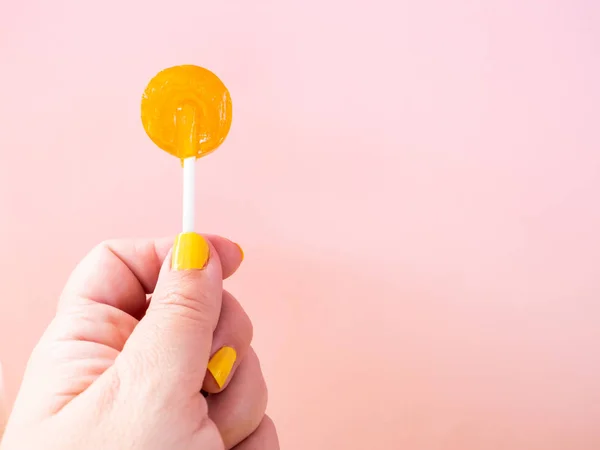 Elinde turuncu lolipop ve pastel pembe arka plan ile sarı boyalı çivi ile bir kadın