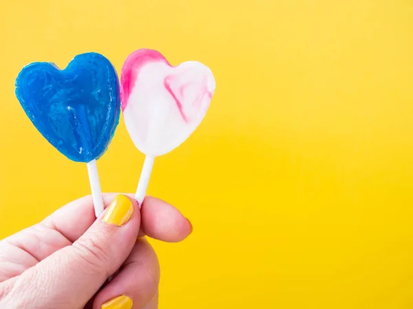 Een vrouw met groen geschilderde nagels met twee verschillende Lollipop in haar hand en gele achtergrond — Stockfoto