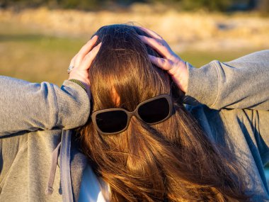 Yüzünün önünde saç ve güneş gözlüğü ile komik jestler yapan kıvrımlı bir kadın
