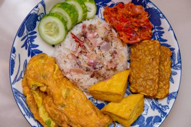 Ev yapımı meşaleli zencefil ya da kecombrang pilavı kızarmış tofu ve tempeh, sambal, omlet ve salatalık ile servis edilir.