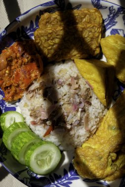 Ev yapımı meşaleli zencefil ya da kecombrang pilavı kızarmış tofu ve tempeh, sambal, omlet ve salatalık ile servis edilir.