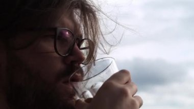 Kahve içen zalim bir adam. Bulutlu bir arkaplan. Sakallı, uzun saçlı makro adam.