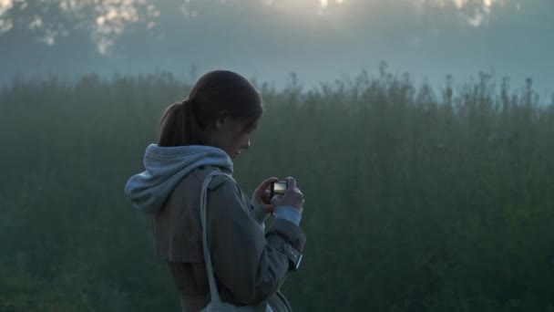 A lány fényképeket készít a reggeli ködről a legelőn. — Stock videók