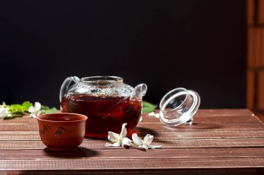 Çaydanlıkta yasemin çiçekleri ve tahta bir masanın üzerinde fincanlar olan doğal çay.