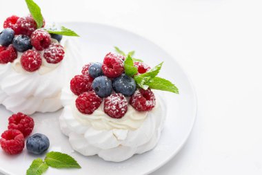 Ahududulu mini Pavlova tatlısı ve beyaz arka planda hintyağı şekerli yaban mersini.