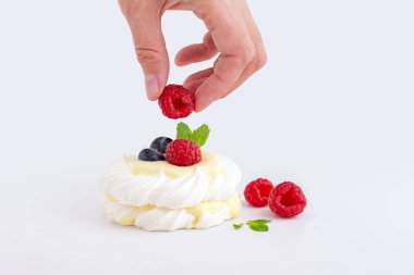 Beyaz arka planda ahududu ve yaban mersinli mini Pavlova tatlısı.