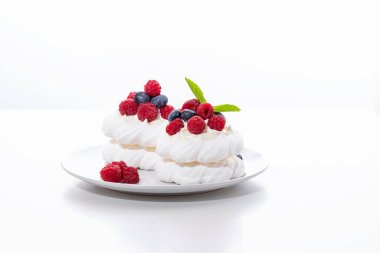 Beyaz arka planda ahududu ve yaban mersinli mini Pavlova tatlısı.