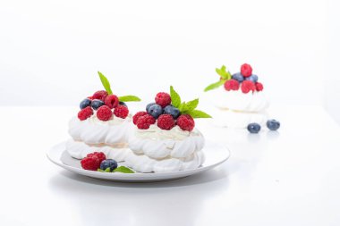 Beyaz arka planda ahududu ve yaban mersinli mini Pavlova tatlısı.