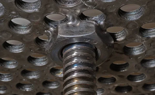 A bottom view of on a bottom part of a chair made from steel nuts welded together. A part of a perforated seat of the chair, leading nut and a support made form a threaded rod. A chair made from many steel nuts and steel rods welded together. The sea