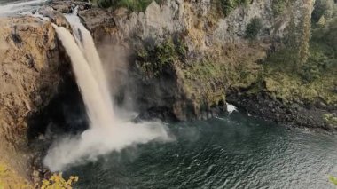 Güçlü bir şelalesi olan doğal manzara nehre dökülüyor, vahşi doğanın güzelliğini ve gücünü vurguluyor..