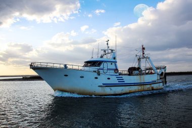 Dolunay ile gün batımında kıyıya dönen balıkçı teknesi
