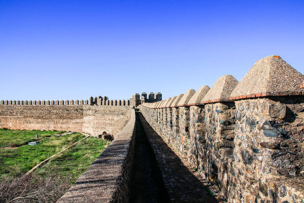 Castle wall with battlement, fortified tower and path in clear and sunny autumn day in a village named "Cumbres Mayores" in Huelva, Andalusia, Spain.