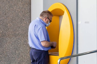 Punta Umbria, Huelva, İspanya - 3 Haziran 2020: ATM makinesinde banka kartı kullanan yaşlı adam Punta Umbria 'da Calle Ancha caddesinde covid-19 koronavirüs nedeniyle koruyucu bir maske takıyor