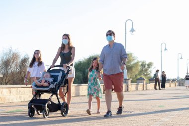 Huelva, İspanya - 3 Haziran 2020: Covid-19 nedeniyle koruyucu maske takan aile gezisi.