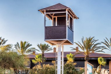 Gün batımında arka planda palmiye ağaçları olan boş kırmızı ahşap cankurtaran kulesi