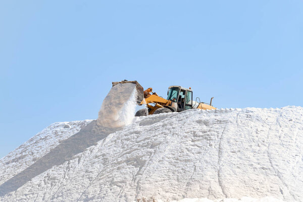 Salt production. Excavator working in a huge pile salt at saltworks. Marine salt produced by the evaporation of seawater.