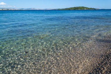 Idyllic çakıl taşı plajı şeffaf su ve canlı mavi deniz nazikçe ufka yaklaşıyor - seyahat, doğa, rahatlama, yaz tatili, arka planlar veya çevre temaları için mükemmel.