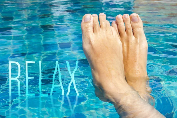 Beautiful female feet relax in clear water. The inscription RELAX