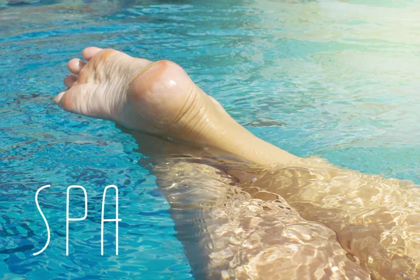 Beautiful female feet relax in clear water. The inscription SPA. Copy space