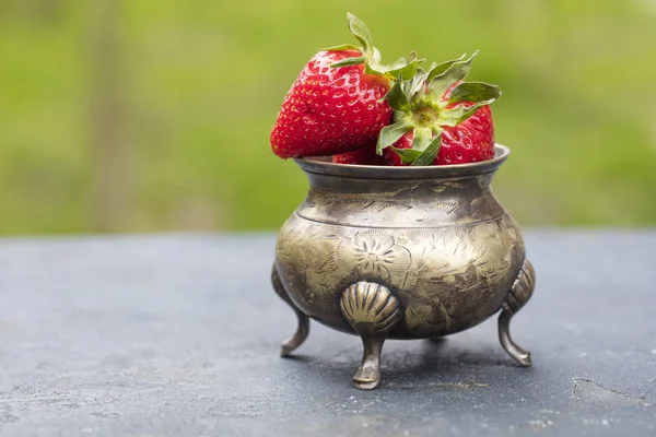 Fresh strawberries in an old, bronze bowl, in the background of nature