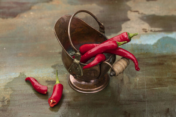 Hot peppers, fresh in a bronze pot, on the wooden background 