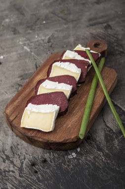 Sertleştirilmiş et ve peynir beyaz kalıp ile. Dilim peynir ve yeşillikleri ile ahşap bir gemide sertleştirilmiş et 