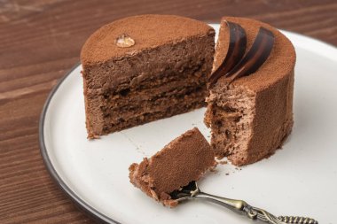 Hafif bir tabak içinde yarım çikolata pasta ile ahşap bir masa üzerinde bir tatlı kaşığı doğranmış. Metniniz için kopya alanı