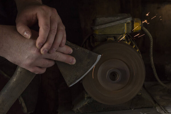 Sharpening the ax in the hands of the man on the grinder. Dark background