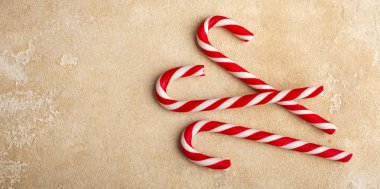 Üç kırmızı ve beyaz çizgili baston şekerler, bej bir masada yalan. Kopya alanı