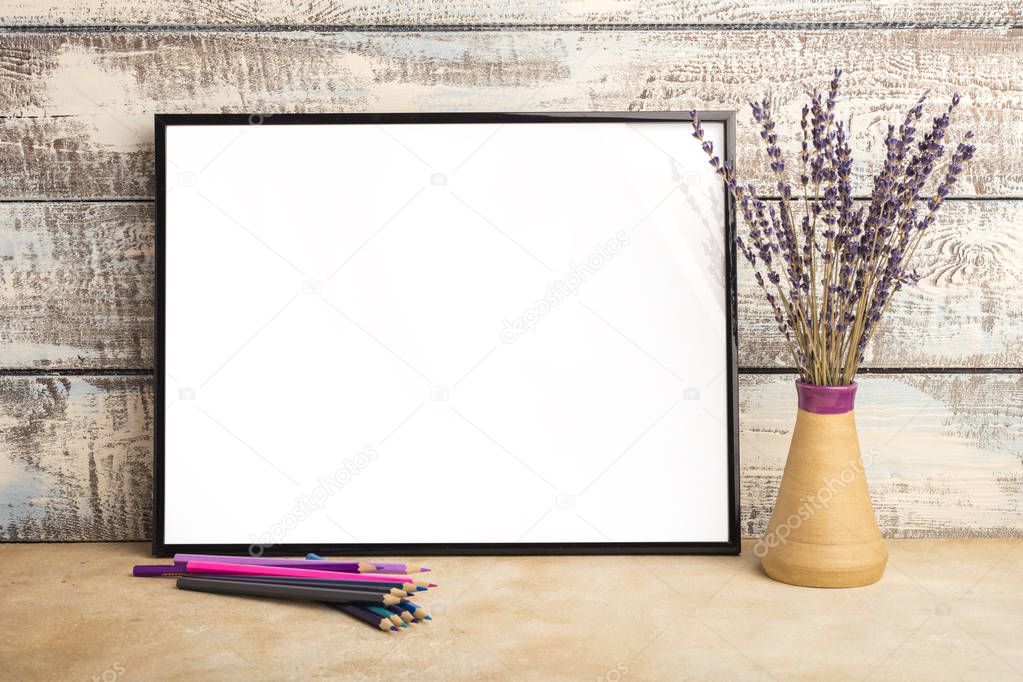 Mock up of an empty frame poster on a wall of wooden boards. A bunch of lavender in a vase and colored pencils on the table
