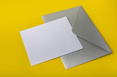 Mock-up harf veya kart ile sarı bir arka plan üzerinde gümüş bir zarf. Kopya alanı