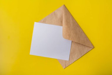 Mock-up mektup ya da kartpostal Kraft zarftan üzerinde sarı bir arka plan ile. Uzay kopyalayın. Yukarıdan görüntülemek