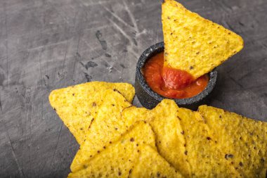 Tortilla mısır cipsi veya Nachos karanlık bir arka plan üzerinde siyah bir kasede sos ile. Kopya alanı  