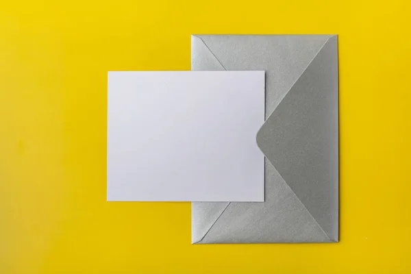 Mock-up letter or card with a silver envelope on a yellow background. Copy space. View from above