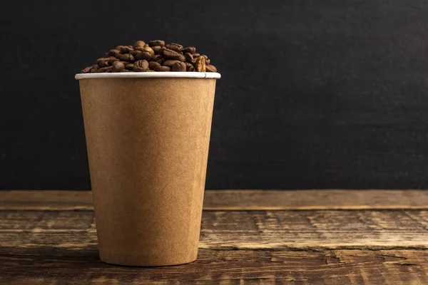 Disposable crafting cup with coffee grains on a wooden table with copy space. Black background. mockup