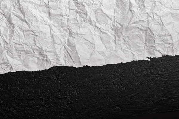 White crumpled paper against a wall in black. View from above