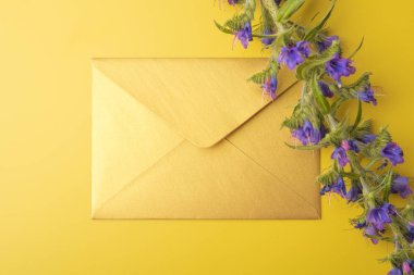 Sarı bir arka plan üzerinde altın bir zarf, mavi çan güzel bir sprig ile. Kopya alanı. Üstte görüntü