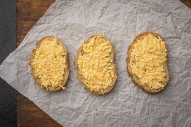 Buruşturulmuş kağıt arka plan üzerinde rendelenmiş peynir ve sarımsak ile Fransız baget üç adet. Üstte görüntü