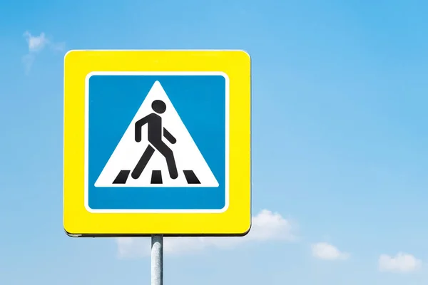 Sign pedestrian crossing with a yellow frame against the blue sky on a sunny day. Copy space