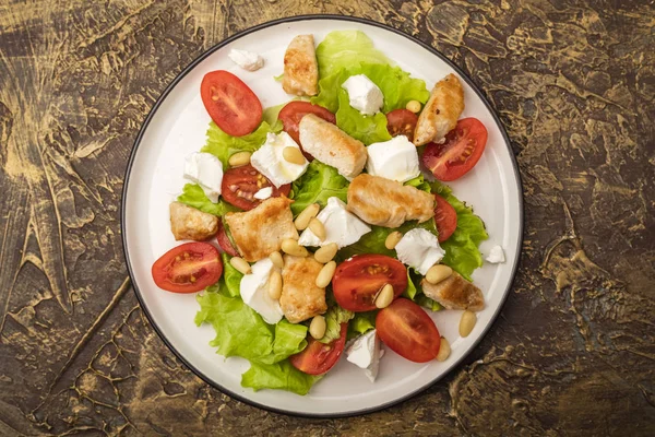 Delicious salad with warm chicken, cherry tomatoes and soft brynza cheese, decorated with pine nuts. dressing with olive oil. dressing with olive oil. Top view