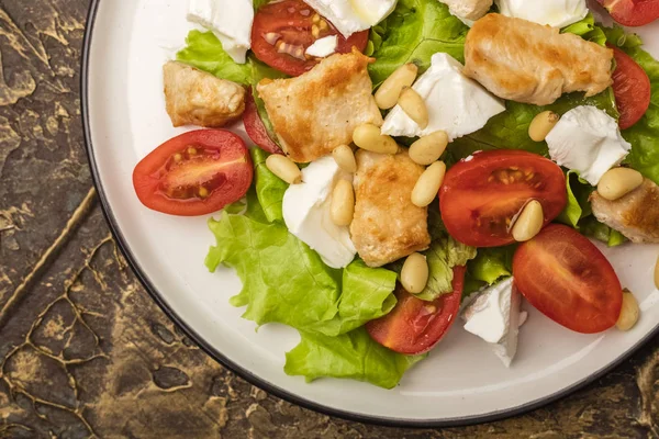 Salad with warm chicken, cherry tomatoes and soft brynza cheese, decorated with pine nuts. dressing with olive oil. dressing with olive oil. Copy space