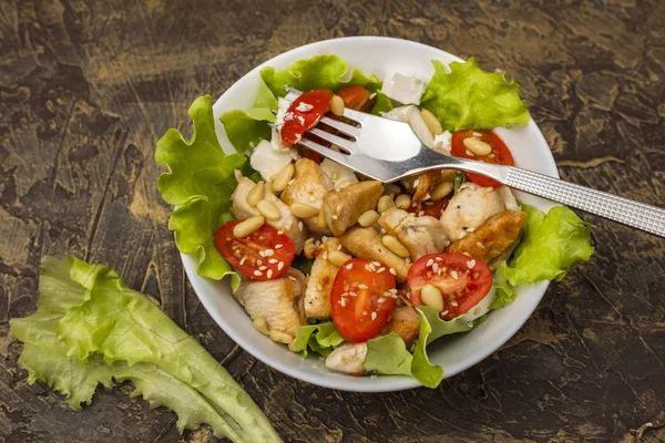 Warm salad with chicken, cherry tomatoes and soft cheese cheese, decorated with pine nuts. dressing with olive oil